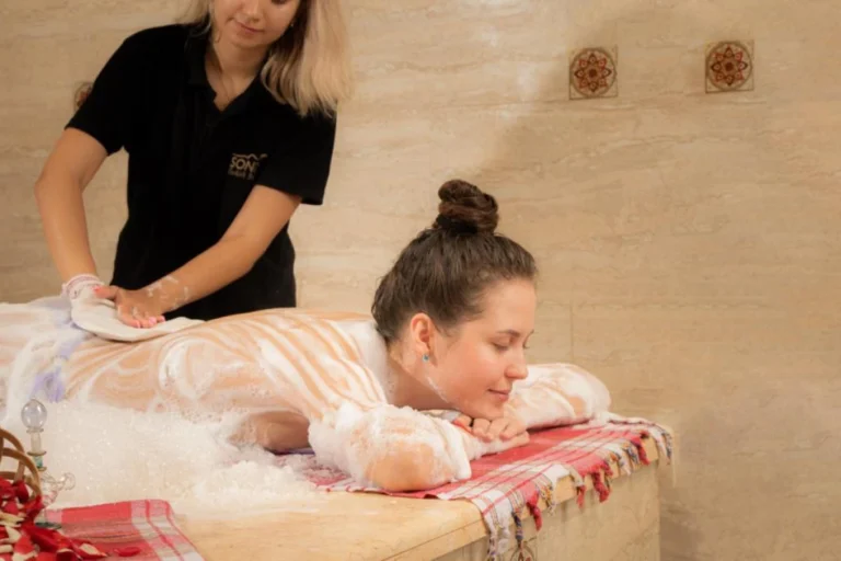СПА Клеопатра плюс с массажем всего тела 45 минут Хургада 46 A full body massage moment for Cleopatra Plus in Hurghada, with white foam covering a client and hands working gently on the back.